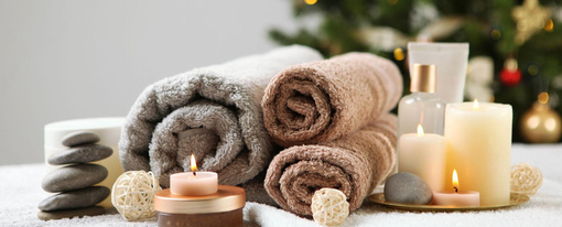 Rolled spa towels, warm stones and candles ready for Christmas spa package in front of a Christmas tree at Earth and Skin day spa - 510x206